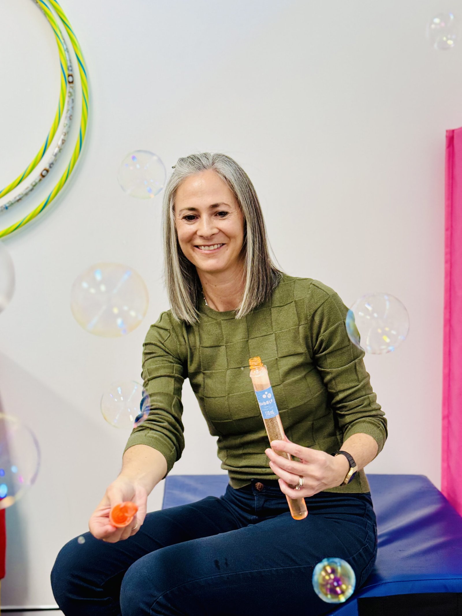 A woman sits on a bench, surrounded by floating bubbles, enjoying a serene moment outdoors.