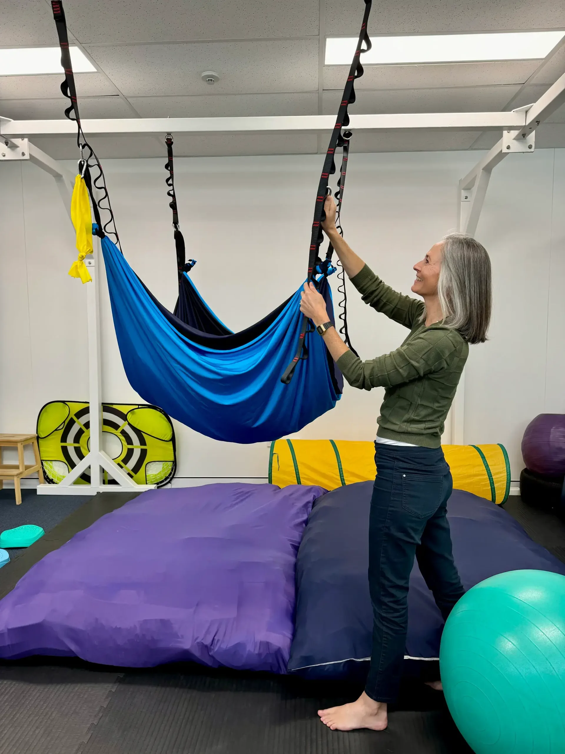 A woman is setting up a hammock indoors, enhancing the room's ambiance with a touch of relaxation and tranquility.