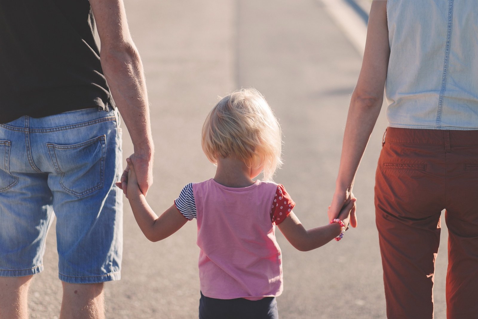 A young girl is seen holding hands with two adults, illustrating a moment of togetherness and familial bond.