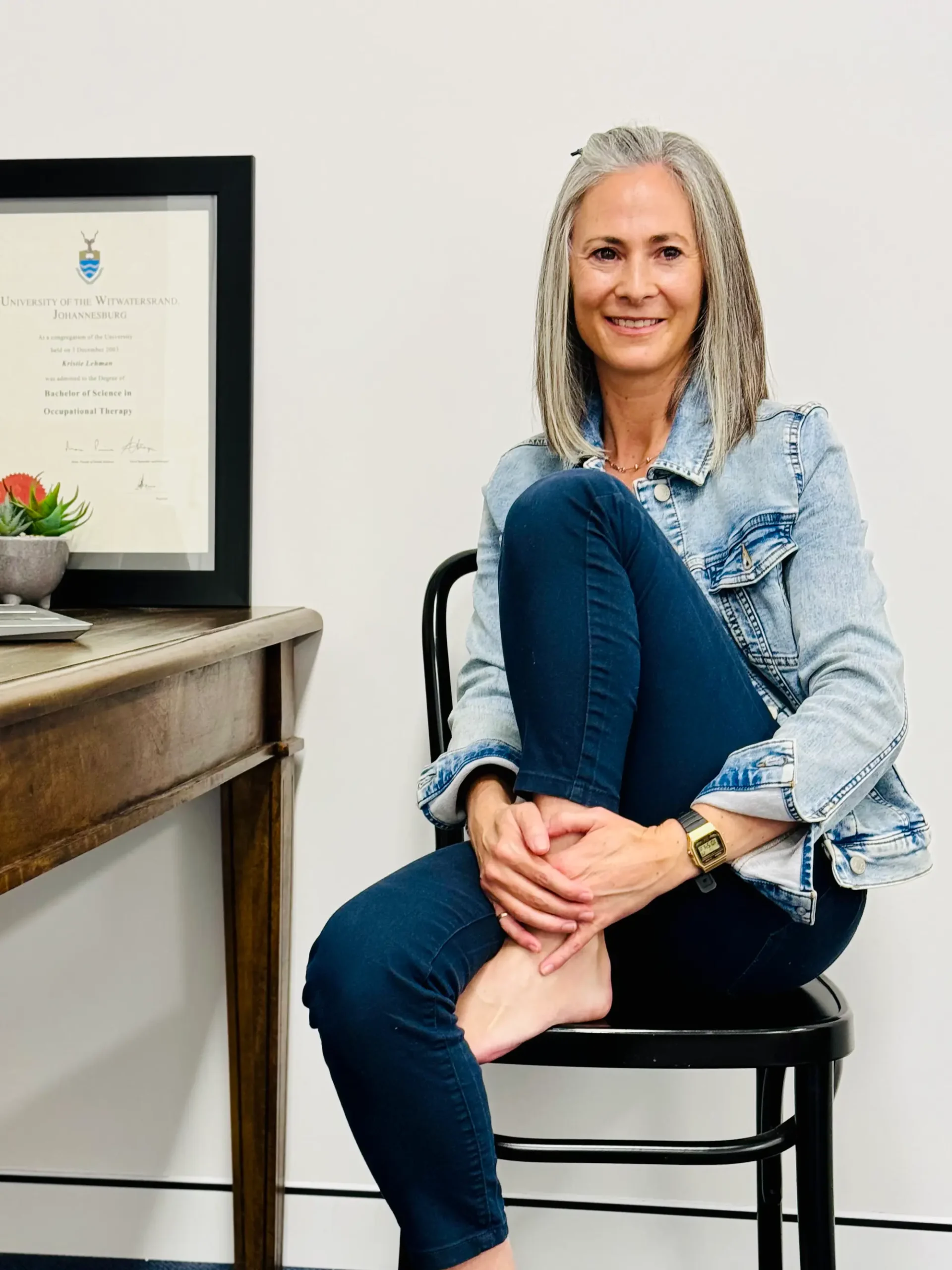 A woman in a chair with a smile, her feet crossed, displaying a relaxed and composed demeanor.