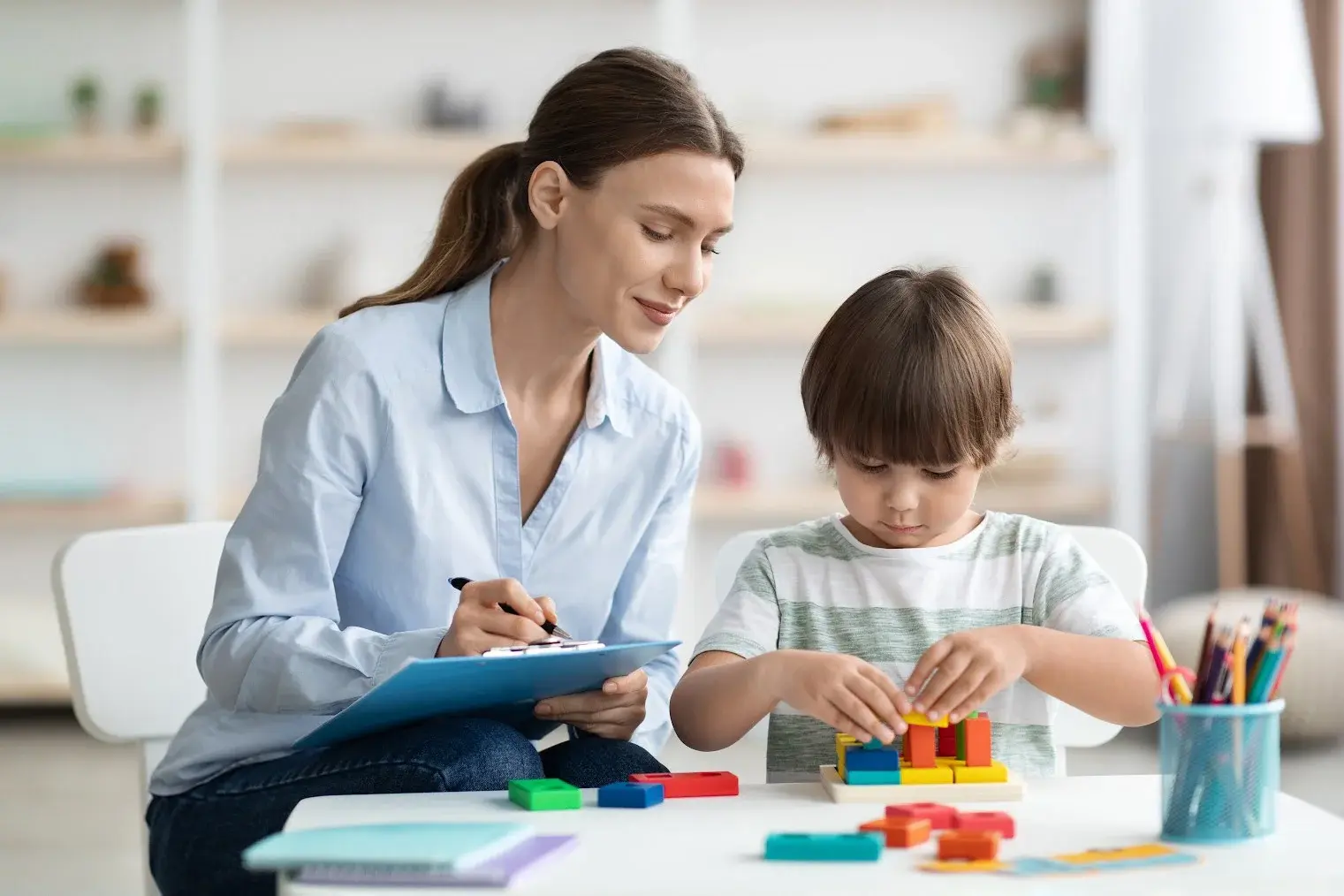 A woman and a child are seated at a table, both focused on a clipboard in front of them.